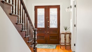 A wooden staircase leading to a double door with a glass panel, a small round table with a plant, and a green doormat. - Raspberry Inn · Classic Riverfront Home-Mins to Woodstock & Skiing (Bridgewater)