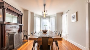 A dining room with a wooden table, chairs, a fireplace, and a hanging light fixture. - Raspberry Inn · Classic Riverfront Home-Mins to Woodstock & Skiing (Bridgewater)