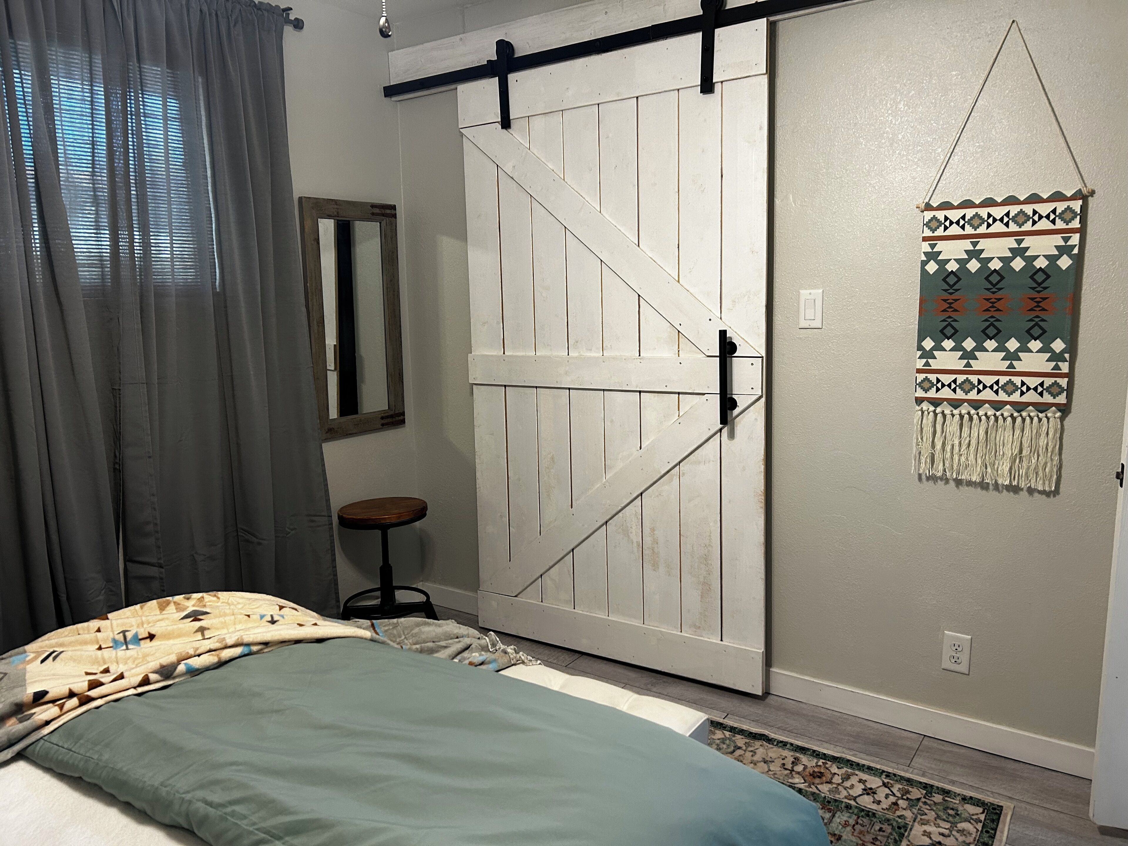 Un dormitorio con cama, una puerta corredera estilo granero, un taburete pequeño, un espejo y un adorno de pared.