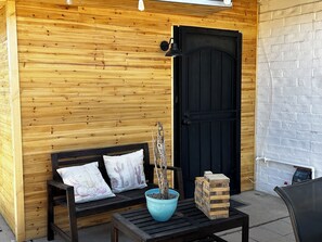 A wooden cabin with a black door, a bench with cactus-themed pillows, a blue pot with a cactus, and a wooden block structure. - Modern Farmhouse in Midtown with fully fenced yard (Tucson)