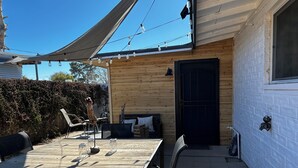 A wooden exterior with a black door, a table with chairs, and string lights. - Modern Farmhouse in Midtown with fully fenced yard (Tucson)