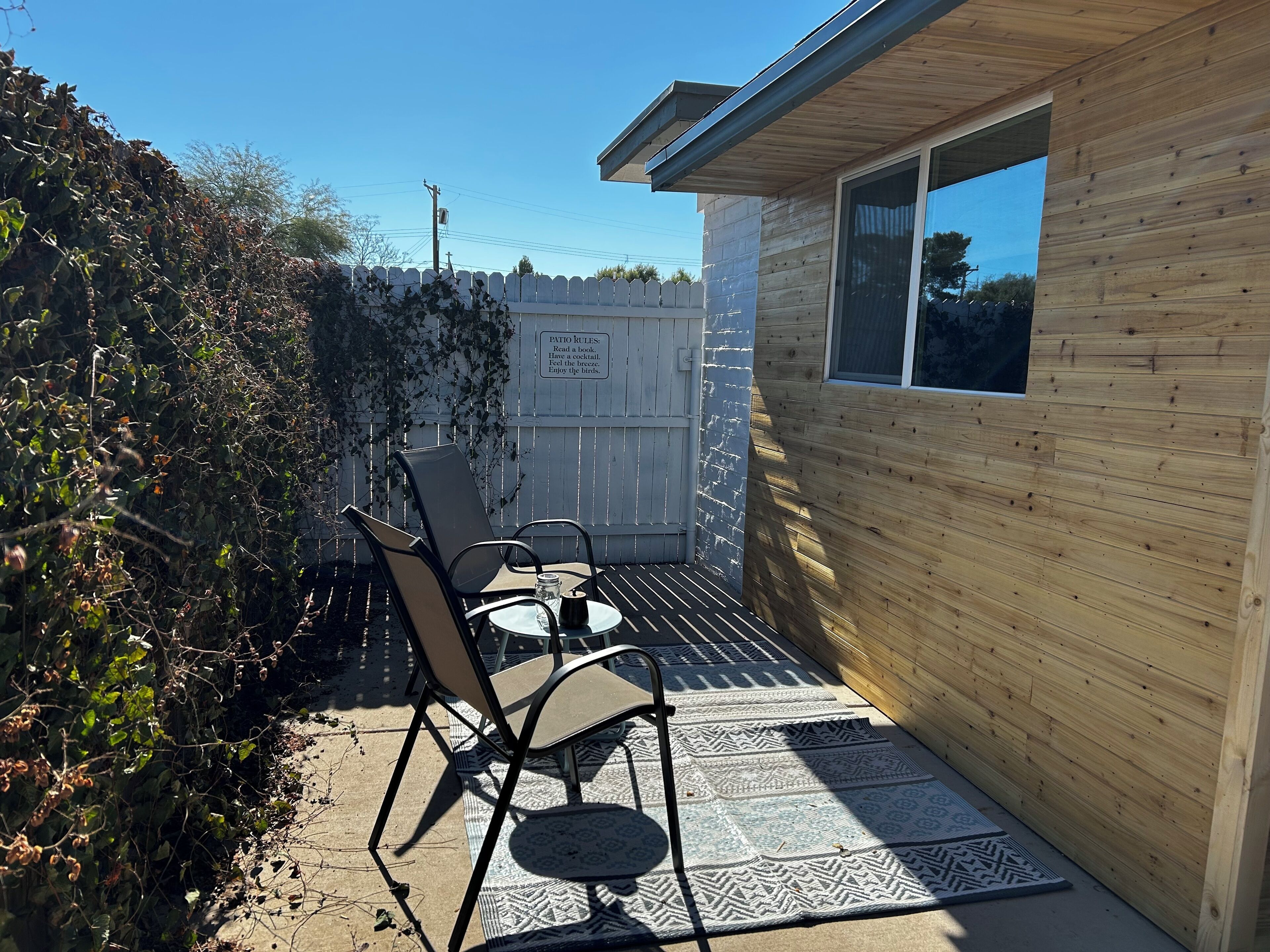 Un patio con dos sillas y una mesa, cerca de una valla de madera y un cartel con las normas del patio.