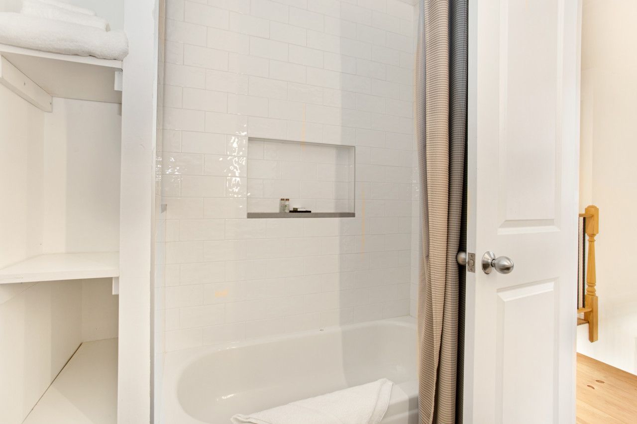 Un baño moderno con ducha de mampara de vidrio, una bañera blanca y una puerta de madera.
