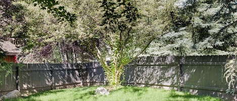 Un patio trasero con un árbol, una cerca de madera y un césped.