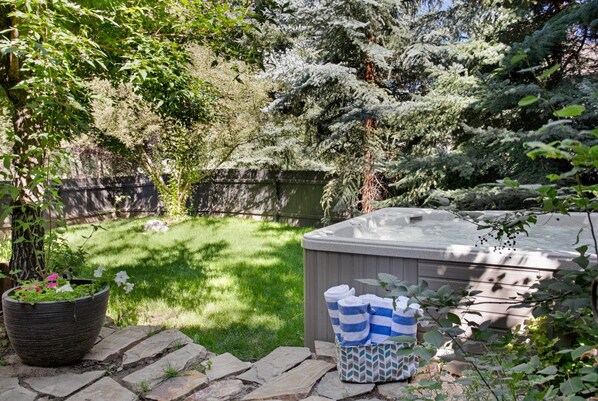 A backyard with a hot tub, a potted plant, and a stone pathway.