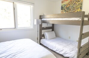 Een stapelbed met een lamp ernaast, een raam en een schilderij aan de muur.
