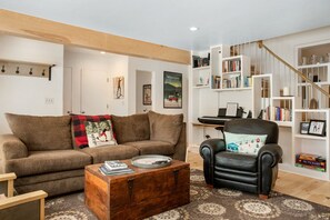 A living room with a brown sofa, a black armchair, a wooden coffee table, and a bookshelf filled with books and decorative items.