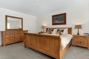 A bedroom with a wooden bed, a dresser, a nightstand, a lamp, and a framed picture on the wall.