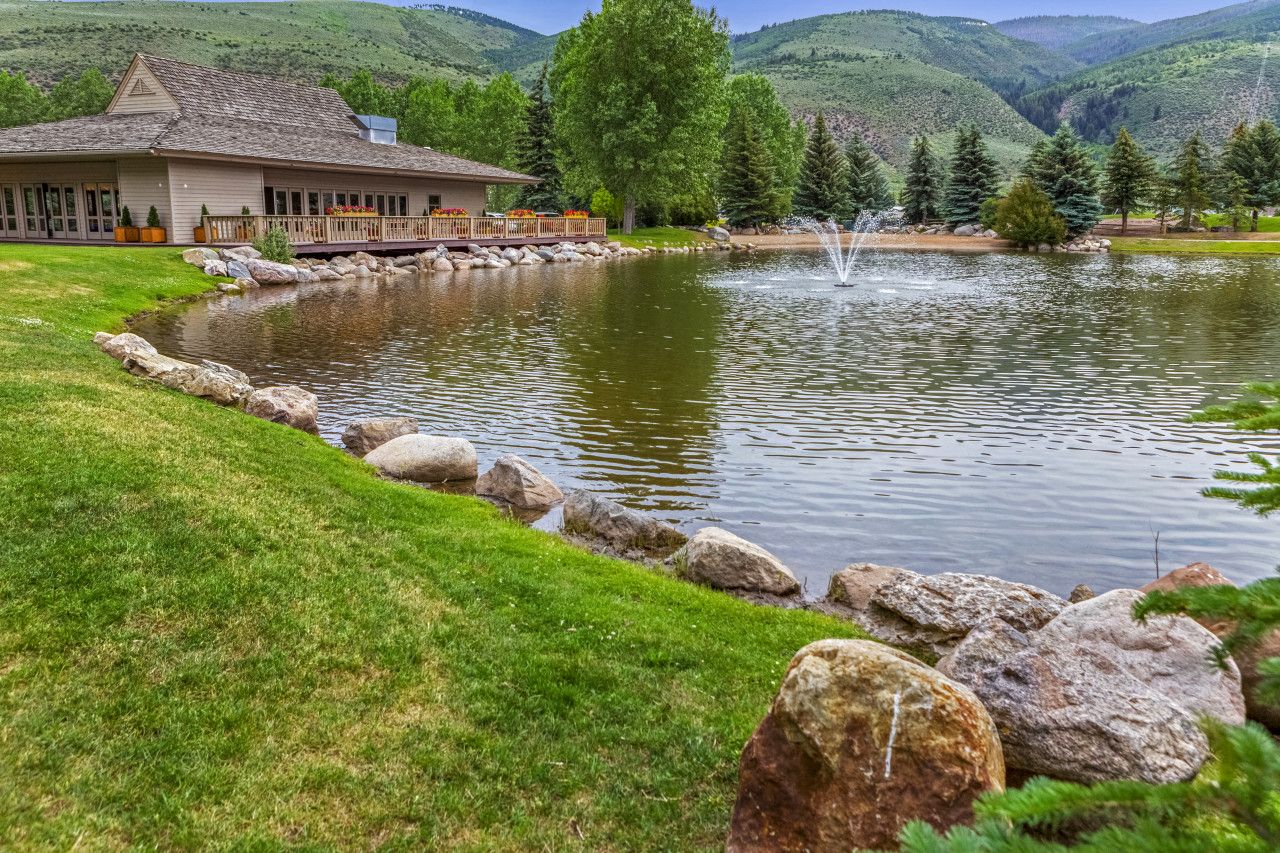 Propiedad junto al lago con un edificio, un estanque con fuente y montañas al fondo.