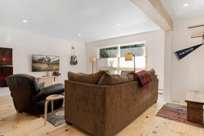A living room with a brown sofa, a black leather chair, a small table, and a guitar on the wall.