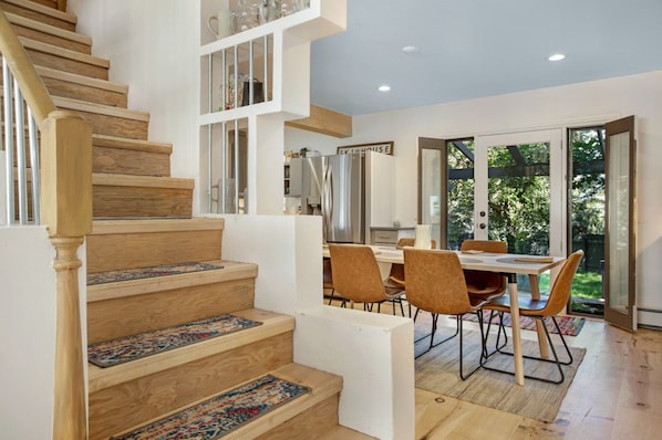 Una cocina moderna con comedor, escalera de madera y vistas al exterior.