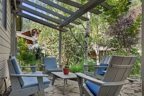 Une terrasse extérieure avec des chaises et une table en bois, entourée de verdure et d’une structure en bois.