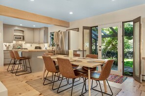 Une cuisine moderne avec un coin repas, comprenant un grand îlot central, des appareils électroménagers intégrés et une porte-fenêtre coulissante donnant sur un jardin.