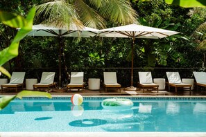 Ein Poolbereich mit Liegestühlen und Sonnenschirmen, umgeben von üppiger Bepflanzung.