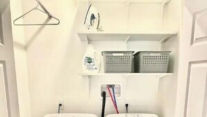 Une buanderie équipée de deux machines à laver blanches, d’un étendoir et d’une étagère où sont rangés des paniers à linge.
