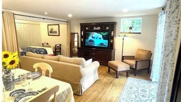 Relax in this stylish living room with a sofa, dining table, and television, offering a view of lush greenery.