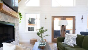 A spacious living room with a stone fireplace, a green sofa, and a large window providing natural light.