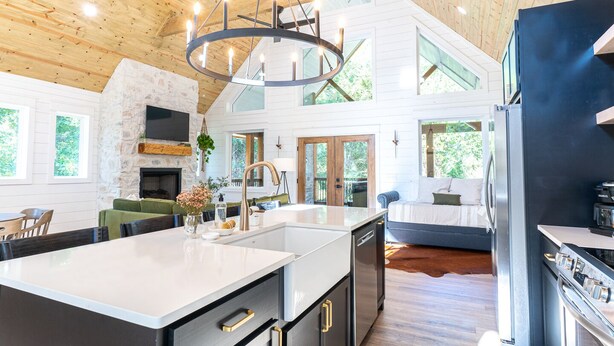 A spacious kitchen with a large island, a stone fireplace, and a modern chandelier.