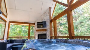 A hot tub area with a stone fireplace, wooden beams, and a view of trees.