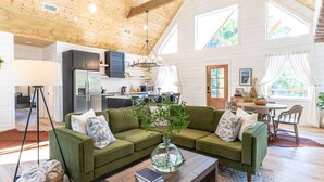 A spacious living area with a green sofa, a coffee table, and a kitchen in the background.