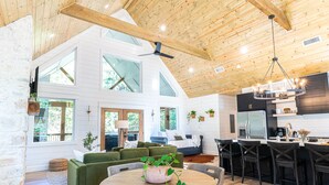 A spacious living area with a high ceiling, large windows, and a modern kitchen with black cabinetry and a central island.