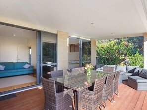 Eine moderne Außenpatio mit einem Glastisch, Korbstühlen und einer Couch.