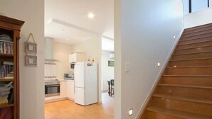 A modern kitchen with white appliances, a wooden staircase, and a hallway leading to a dining area. - Great family holiday home with entertainment area for extras (Bowentown)