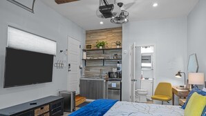 Ett kompakt hotellrum med en säng, en TV, ett litet kök och ett badrum.