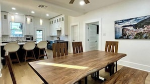 A modern kitchen with white cabinets, a dining area with a wooden table and chairs, and a ceiling fan.