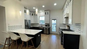 A modern kitchen with white cabinets, a central island, and a dining area with white chairs.