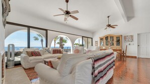 A spacious living room with white furniture, large windows, and a view of the ocean. - Beachfront Villa + Casitas w/ pool. 6 BR (Los Barriles)