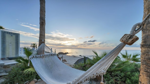 A hammock tied between two palm trees on a beach with a view of the ocean and a building in the background. - Beachfront Villa + Casitas w/ pool. 6 BR (Los Barriles)
