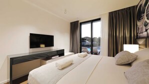 A modern hotel room with a large bed, a flat-screen TV, a desk, and a view of the outdoors.