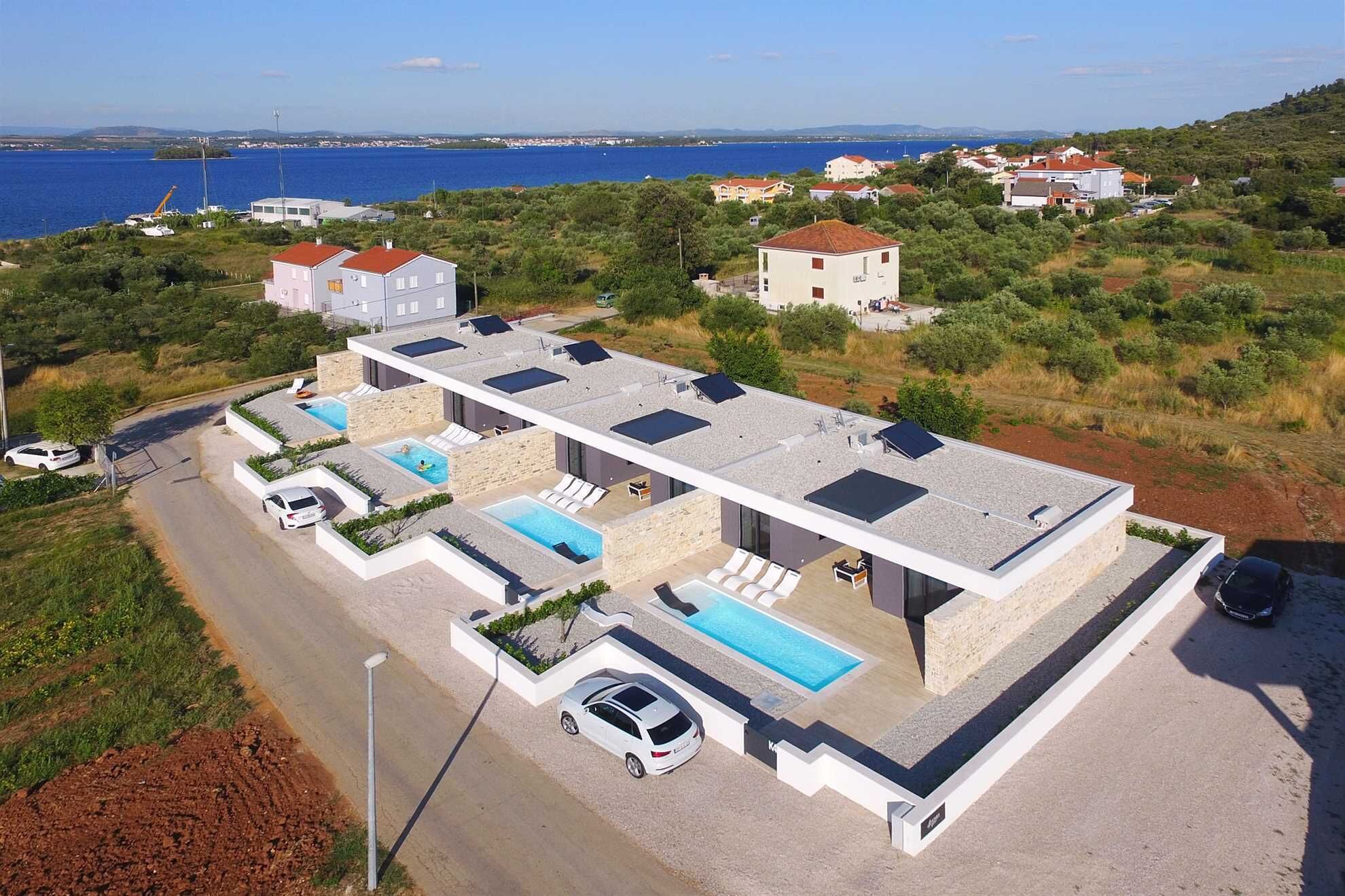 Una villa moderna con piscina en la azotea, rodeada de vegetación y vistas al mar.