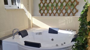 A hot tub with a wooden lattice wall behind it, a window with blinds, and a small plant on the right. - Acropolis Lux 2 Bedroom Apt,CBD, H/TUB, fast Wifi-1min from Museum&Metro station (Athens)
