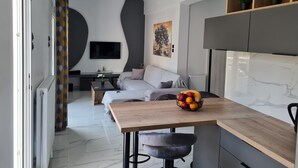 A modern kitchen with a marble countertop, a dining table with a fruit bowl, and a grey sofa in the background. - Acropolis Lux 2 Bedroom Apt,CBD, H/TUB, fast Wifi-1min from Museum&Metro station (Athens)