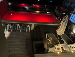 A pool area with a red-lit pool, white lounge chairs, and a wooden deck. - HOTEL PIEDRA SANTA - Moquegua (Moquegua)