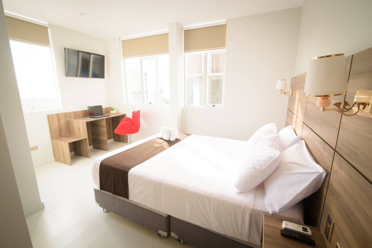 Ein modernes Hotelzimmer mit einem großen Bett, einem Schreibtisch, einem Fernseher und einem Fenster mit Jalousien.