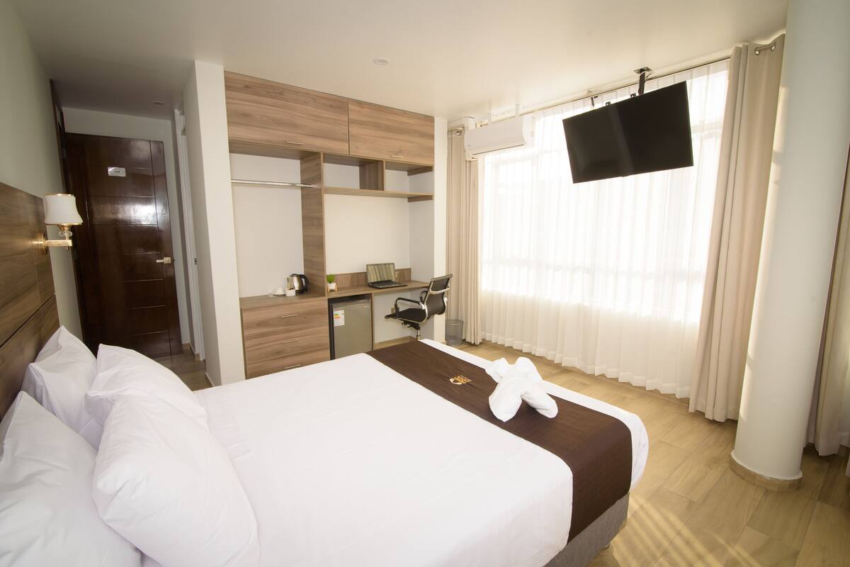 Ein Hotelzimmer mit Bett, Schreibtisch, Fernseher und einem Fenster mit Vorhängen.