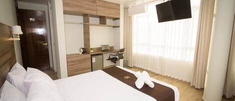 A hotel room with a bed, a desk, a TV, and a window with curtains.