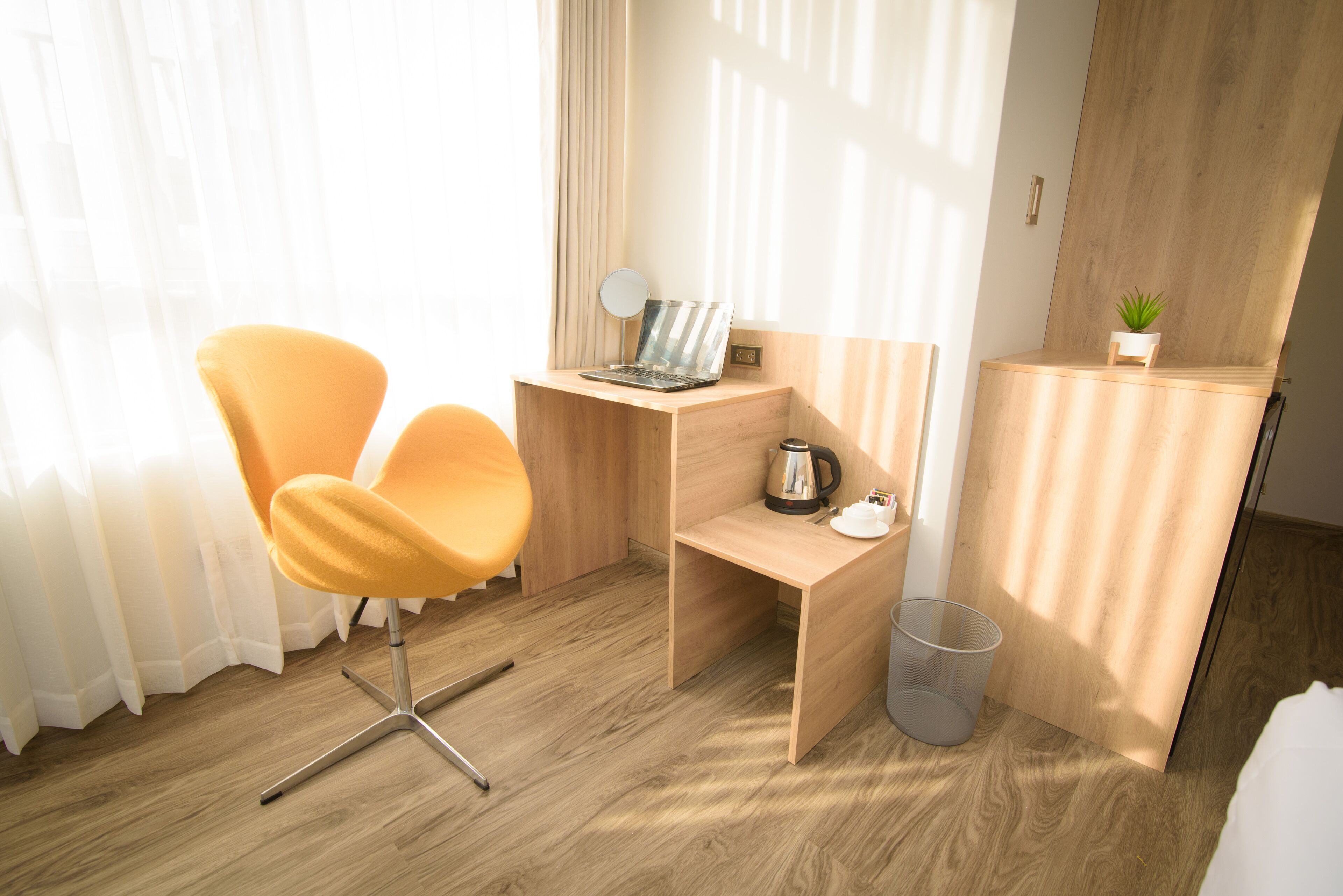 A modern hotel room with a wooden desk, a laptop, a coffee maker, and a small plant.
