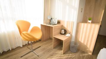 A modern hotel room with a wooden desk, a laptop, a coffee maker, and a small plant.
