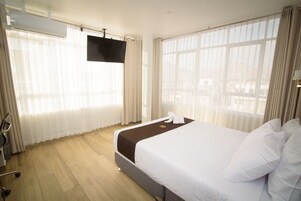 Habitación de hotel con una cama grande, un televisor de pantalla plana en la pared y vistas a la ciudad a través de las ventanas.
