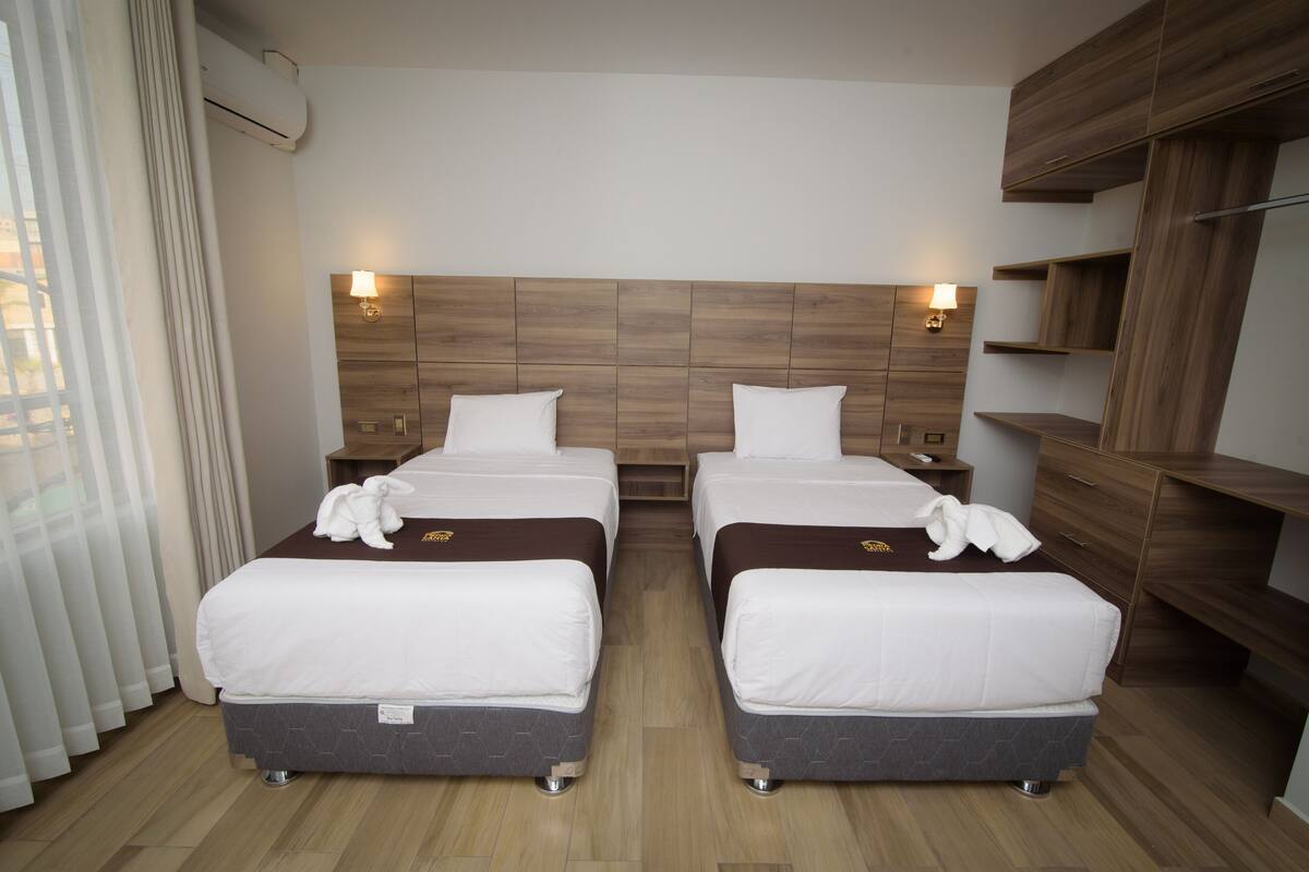 Ein Hotelzimmer mit zwei Betten, einem Holzkopfende, Nachttischen und einer eingebauten Regaleinheit.