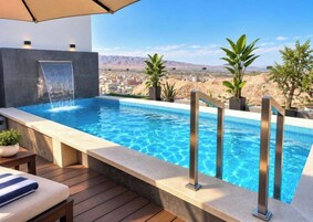 Una piscina con cascada, rodeada de plantas en macetas y con vistas a un paisaje montañoso.