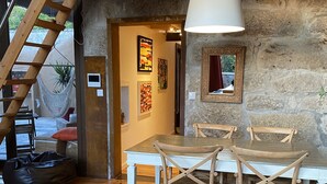 Uma zona de refeições rústica com uma mesa e cadeiras de madeira, uma planta pendente e uma parede de pedra.