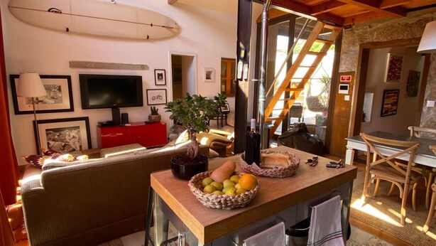 Uma sala de estar aconchegante com uma mesa de jantar de madeira, televisão e escada que leva a um andar superior.