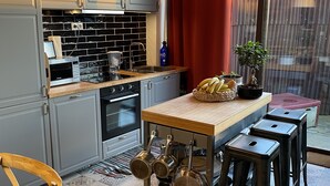 Cozinha compacta com armários cinza, bancada de madeira e área de refeições com banquetas.