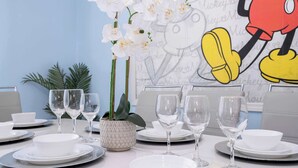 Ein Esstisch ist gedeckt mit weißen Tellern, Schüsseln und Weingläsern, dazu gehören weiße Orchideen und ein Topfpflanze.