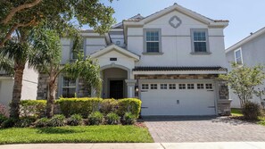 A two-story house with a stone facade, a garage, and a well-maintained front yard with various plants. - Champions Gate Mansion with Private Pool (Four Corners)